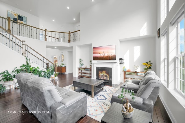 living area featuring a high ceiling, stairway, recessed lighting, wood finished floors, and a glass covered fireplace
