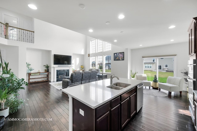 kitchen with light countertops, dark brown cabinets, dark wood-type flooring, dishwasher, and a sink