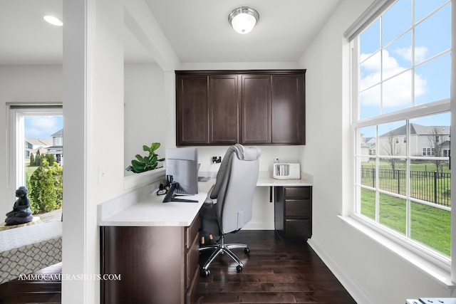 home office with dark wood-type flooring, built in study area, and baseboards