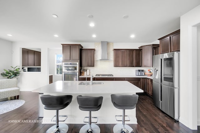 kitchen featuring dark brown cabinetry, wall chimney range hood, light countertops, stainless steel appliances, and a sink