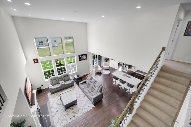 living area with recessed lighting, a high ceiling, wood finished floors, stairs, and baseboards