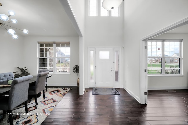 foyer entrance featuring a high ceiling, baseboards, a chandelier, and dark wood-style floors