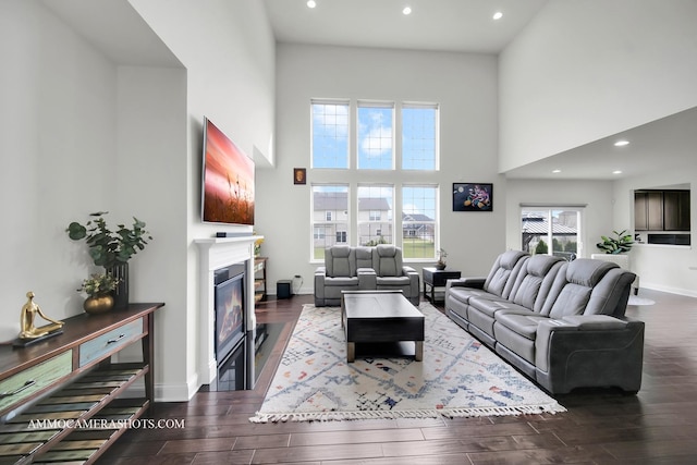 living area with recessed lighting, wood finished floors, a glass covered fireplace, and a towering ceiling