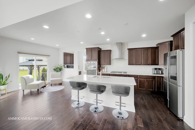 kitchen featuring tasteful backsplash, wall chimney exhaust hood, light countertops, stainless steel appliances, and a breakfast bar area