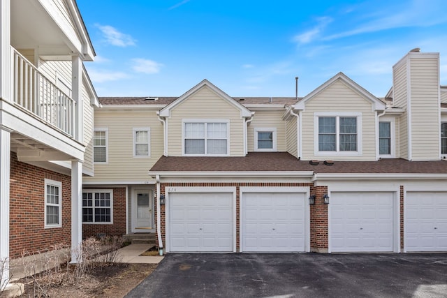 townhome / multi-family property featuring driveway, a shingled roof, a garage, and brick siding