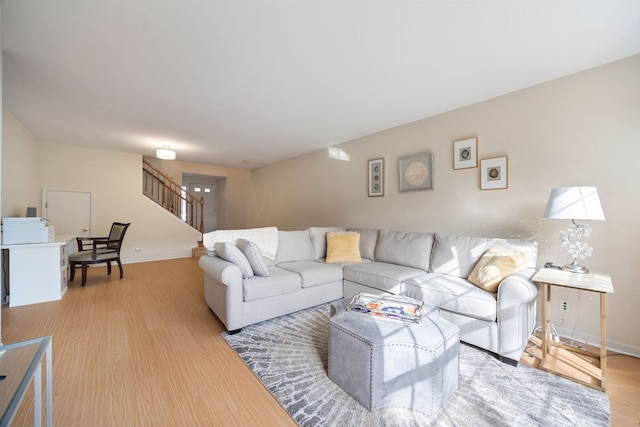 living area with stairs, light wood-style floors, and baseboards