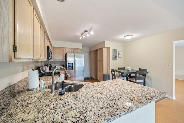 kitchen with light brown cabinetry, a sink, light stone counters, a peninsula, and appliances with stainless steel finishes