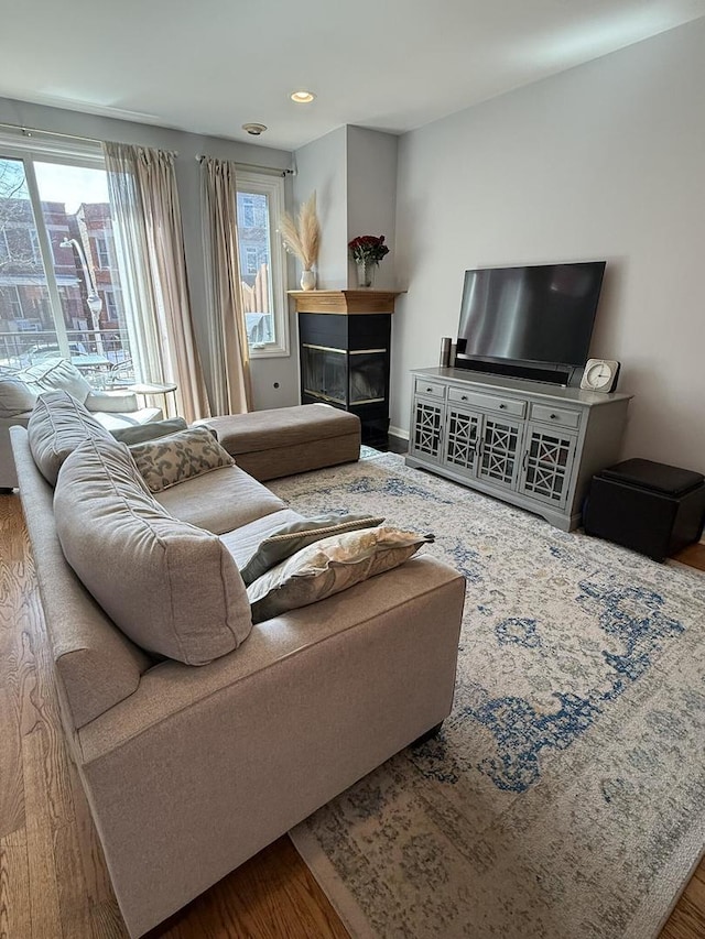 living area featuring a glass covered fireplace, recessed lighting, wood finished floors, and a healthy amount of sunlight
