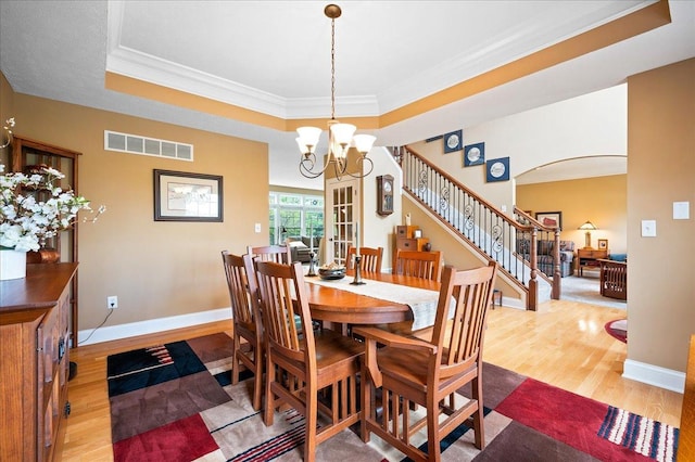dining space featuring light wood finished floors, visible vents, stairs, a chandelier, and arched walkways