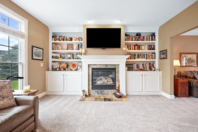 carpeted living area with baseboards, a tile fireplace, and built in shelves