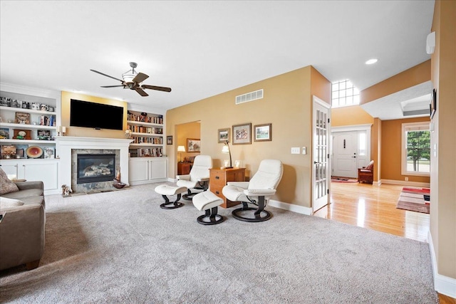 carpeted living area with a ceiling fan, baseboards, a glass covered fireplace, visible vents, and built in features