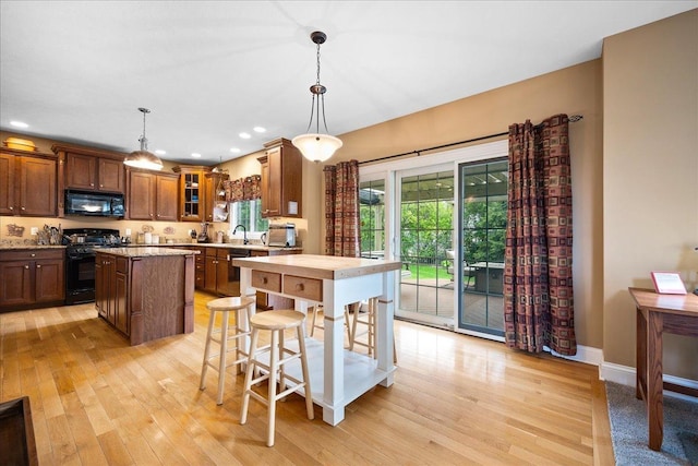 kitchen featuring black appliances, light wood-style floors, glass insert cabinets, and a kitchen island