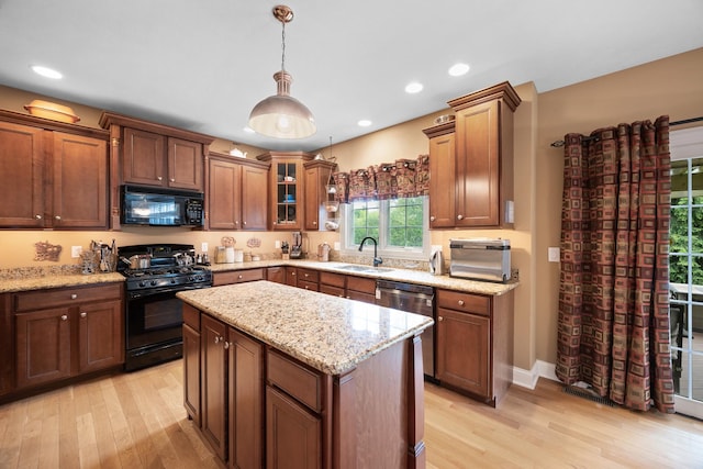 kitchen with a sink, light wood finished floors, decorative light fixtures, and black appliances