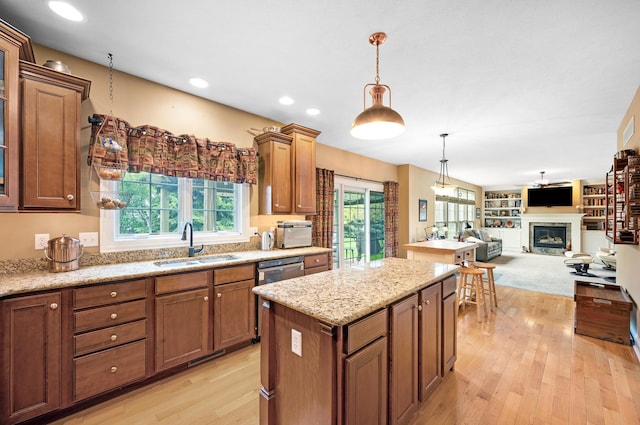 kitchen with a center island, a sink, pendant lighting, a glass covered fireplace, and light wood-style floors