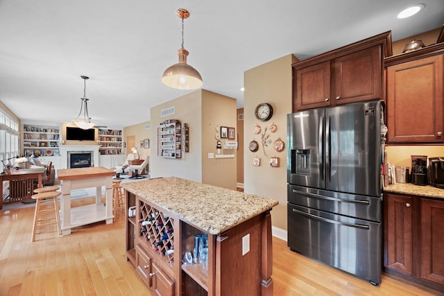 kitchen featuring stainless steel refrigerator with ice dispenser, visible vents, light wood finished floors, hanging light fixtures, and a kitchen island