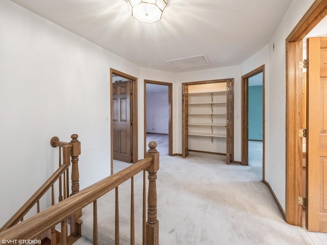hallway featuring attic access, light colored carpet, baseboards, and an upstairs landing
