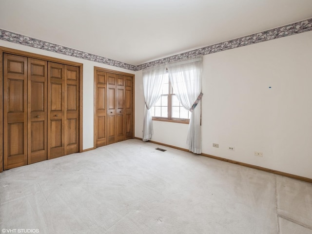 unfurnished bedroom with two closets, visible vents, baseboards, and light colored carpet
