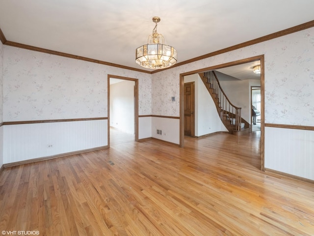 spare room featuring a chandelier, light wood finished floors, stairway, wallpapered walls, and a wainscoted wall