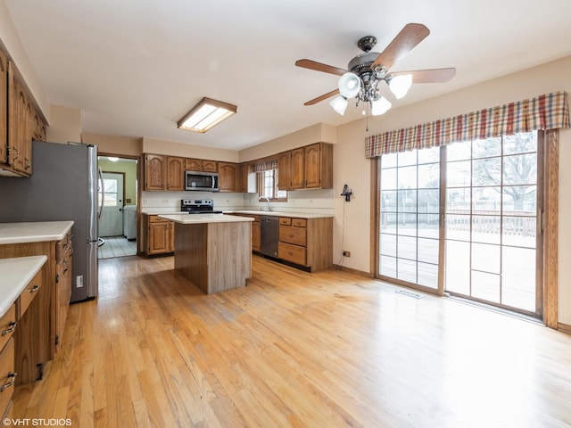 kitchen featuring a center island, washer and dryer, appliances with stainless steel finishes, light wood-type flooring, and brown cabinetry