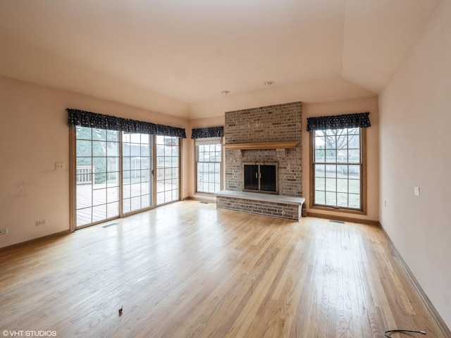 unfurnished living room with visible vents, a wealth of natural light, a brick fireplace, and wood finished floors