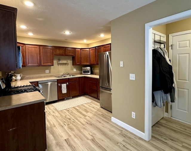 kitchen featuring light countertops, stainless steel appliances, baseboards, a sink, and light wood finished floors