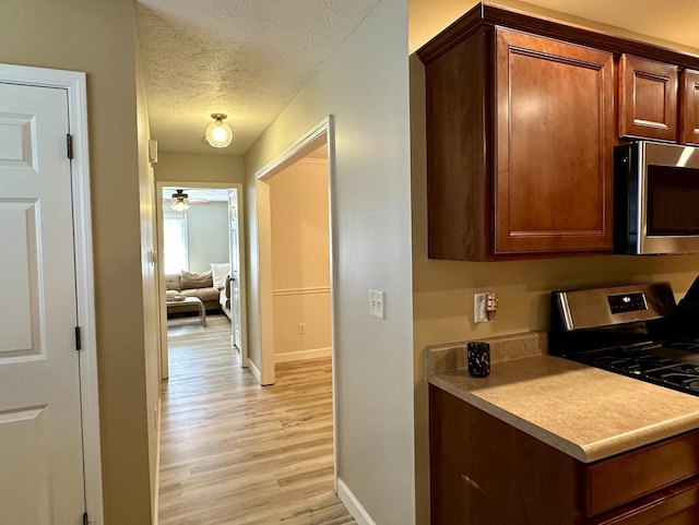 kitchen featuring a textured ceiling, baseboards, ceiling fan, appliances with stainless steel finishes, and light wood-style floors