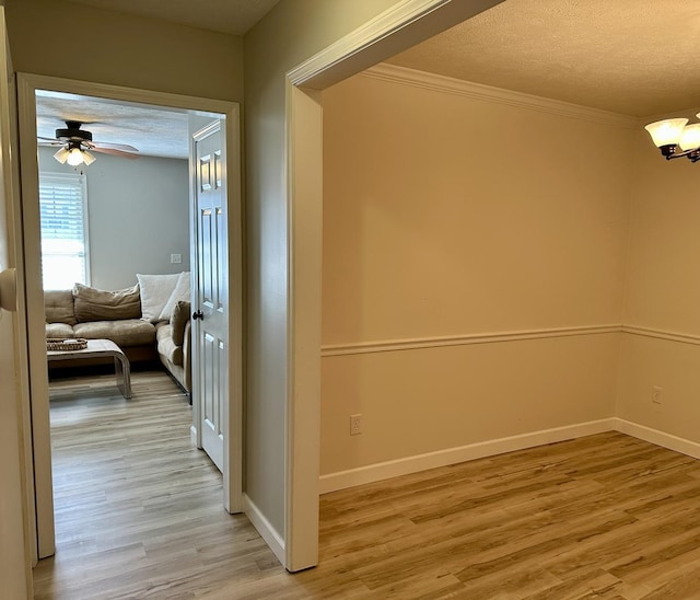 hall featuring ornamental molding, baseboards, light wood finished floors, and a textured ceiling