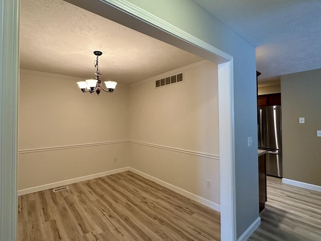 unfurnished dining area featuring a notable chandelier, crown molding, light wood-style flooring, baseboards, and visible vents