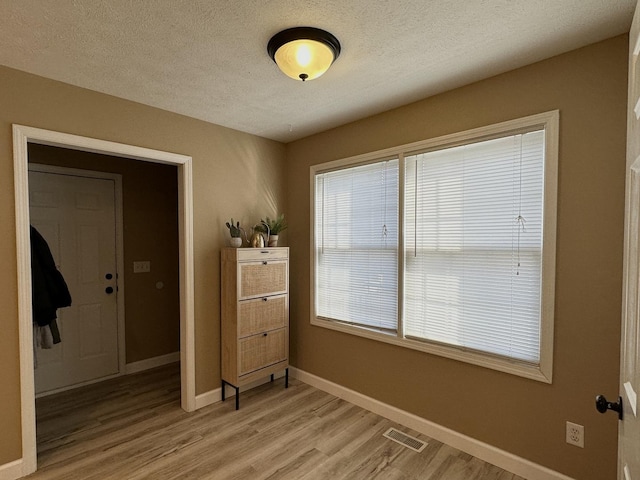 empty room featuring a textured ceiling, baseboards, light wood finished floors, and visible vents