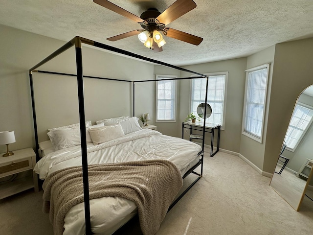 bedroom with a ceiling fan, light carpet, multiple windows, and a textured ceiling