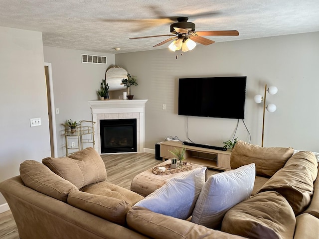 living room with a textured ceiling, visible vents, light wood finished floors, a fireplace, and a ceiling fan