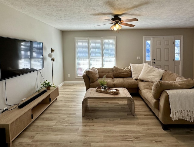 living room featuring a textured ceiling, ceiling fan, baseboards, and light wood-type flooring