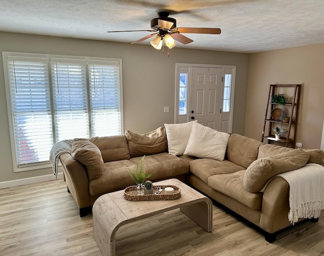 living area featuring baseboards, a textured ceiling, light wood-style floors, and a ceiling fan