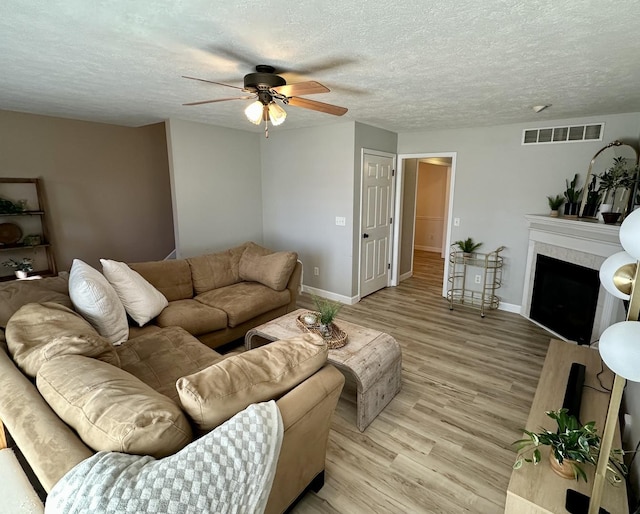 living room with light wood-type flooring, a ceiling fan, a textured ceiling, and visible vents