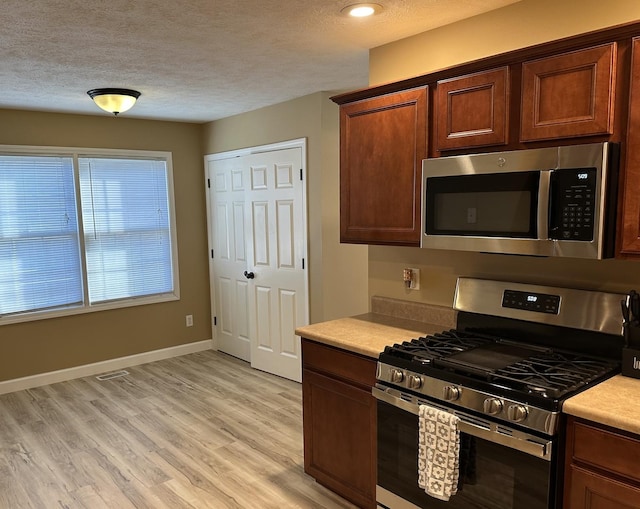 kitchen with light countertops, a textured ceiling, light wood-style flooring, stainless steel appliances, and baseboards