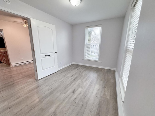 unfurnished room with a baseboard heating unit, baseboards, and wood finished floors