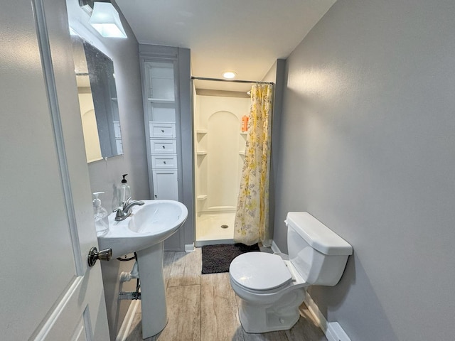 bathroom featuring toilet, a stall shower, wood finished floors, and baseboards