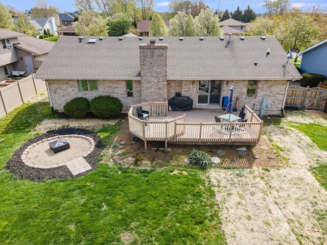 back of property with brick siding, a deck, roof with shingles, and an outdoor fire pit