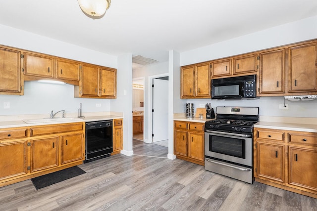 kitchen with light countertops, brown cabinetry, a sink, and black appliances