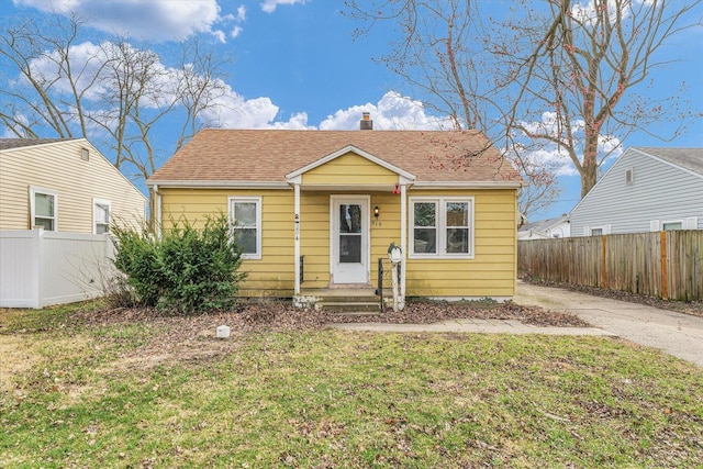 bungalow-style house with fence, roof with shingles, concrete driveway, and a front yard
