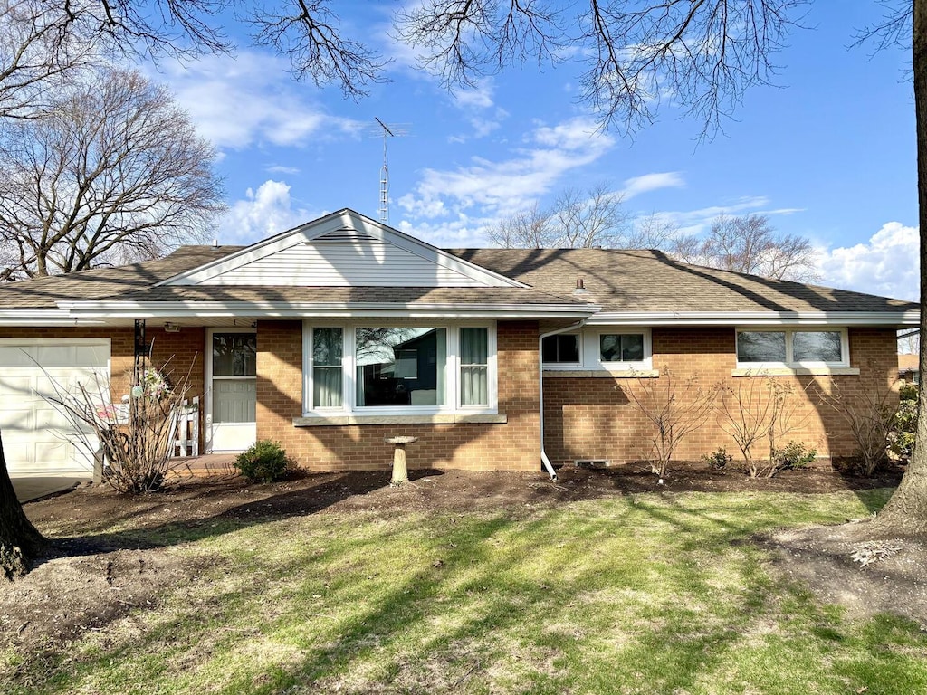 ranch-style home featuring brick siding, a garage, roof with shingles, and a front lawn