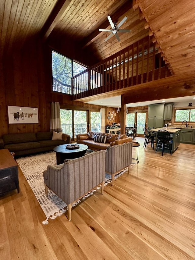 living room featuring wooden ceiling, beam ceiling, a ceiling fan, wood walls, and light wood-type flooring