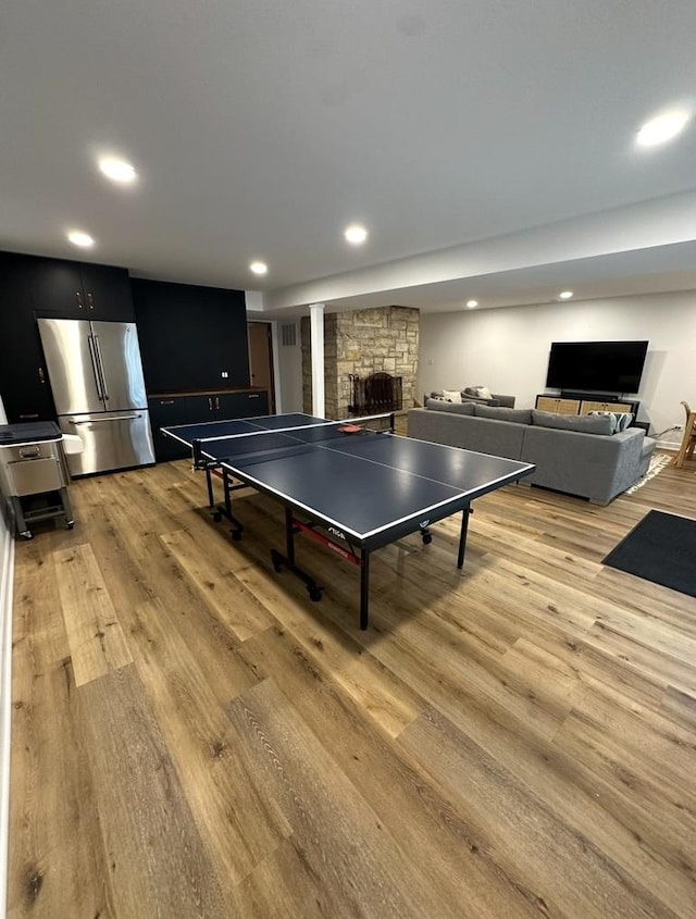 rec room featuring a stone fireplace, light wood finished floors, and recessed lighting