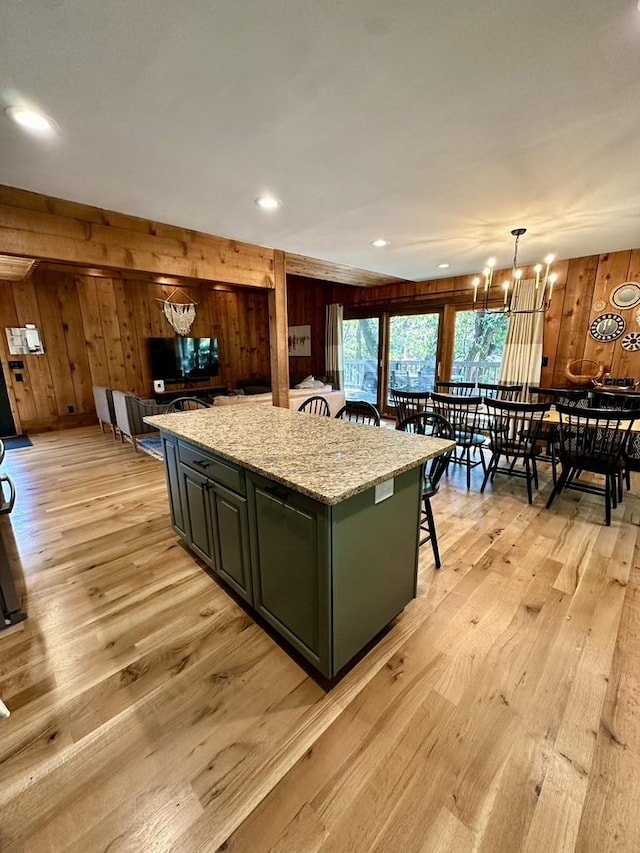 kitchen featuring light wood-style flooring, wooden walls, a kitchen bar, an inviting chandelier, and a center island