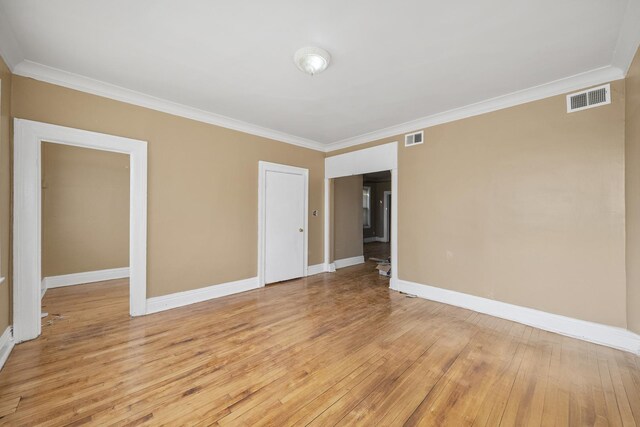 empty room with baseboards, crown molding, light wood-style floors, and visible vents