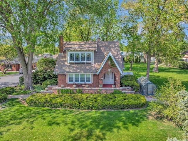 english style home with a chimney, a front yard, brick siding, and an outbuilding