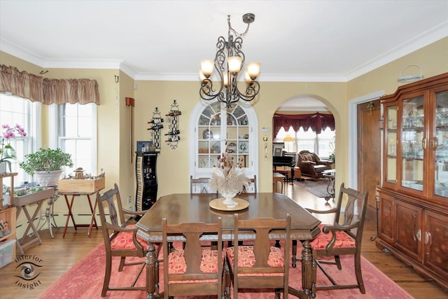 dining room with light wood-style flooring, arched walkways, a chandelier, and ornamental molding