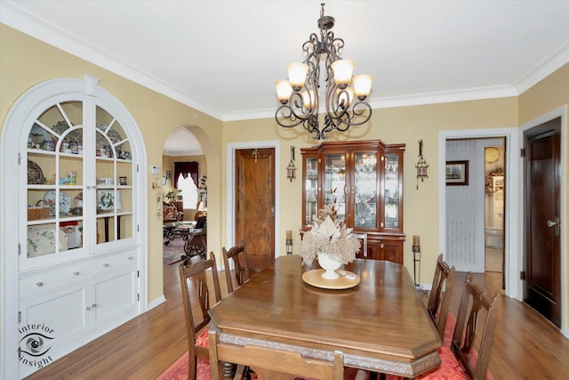 dining area featuring arched walkways, a chandelier, wood finished floors, and ornamental molding