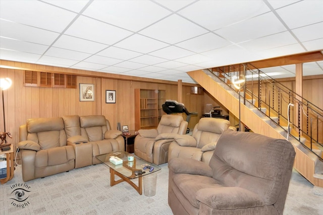 living room with wooden walls, a drop ceiling, carpet, and stairway
