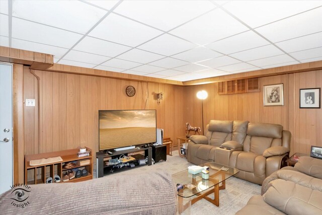 carpeted living area featuring wood walls and a drop ceiling